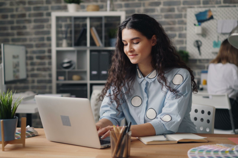 Professional woman using a laptop to update her resume in a modern office workspace.