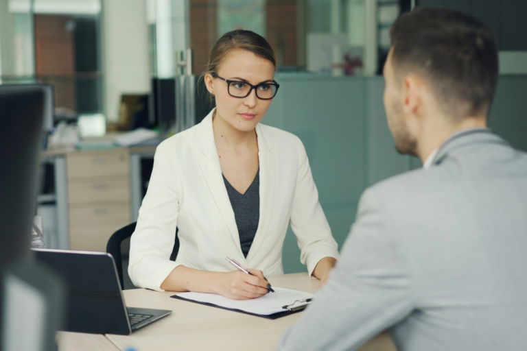 A professional female interviewer listening to a male job candidate during an interview in a modern office.