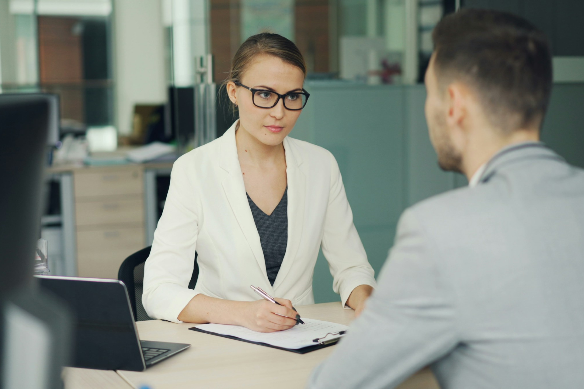 A professional female interviewer listening to a male job candidate during an interview in a modern office.