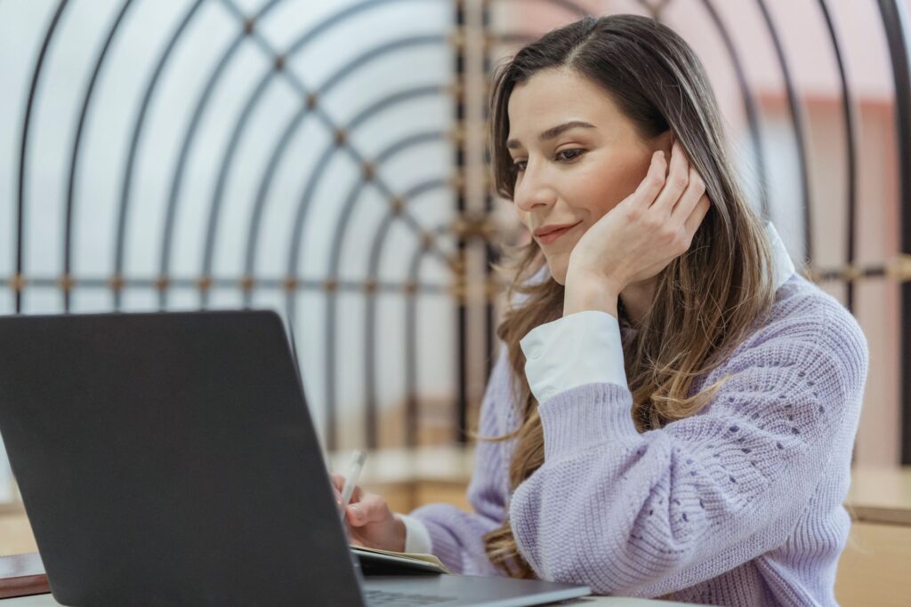 A woman working on a laptop and notebook while preparing answers for behavioral interview questions