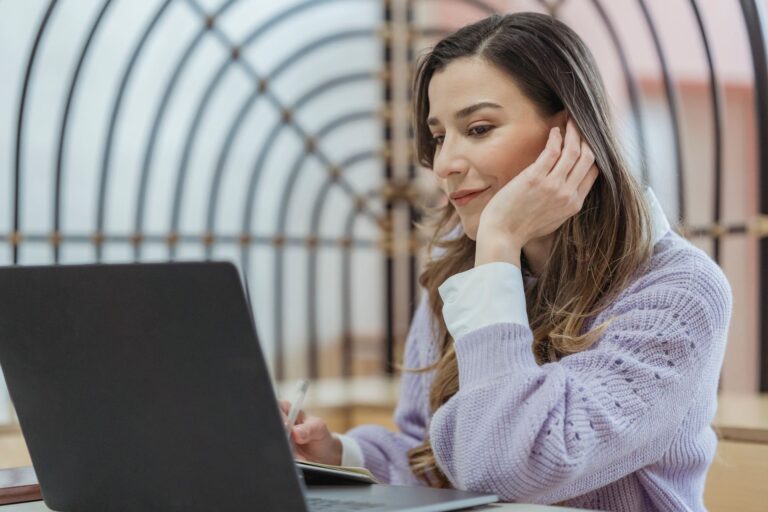 A woman working on a laptop and notebook while preparing answers for behavioral interview questions
