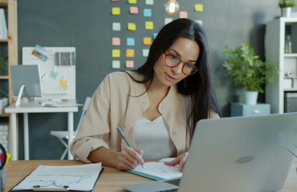 Professional woman taking notes while researching job search strategies on a laptop