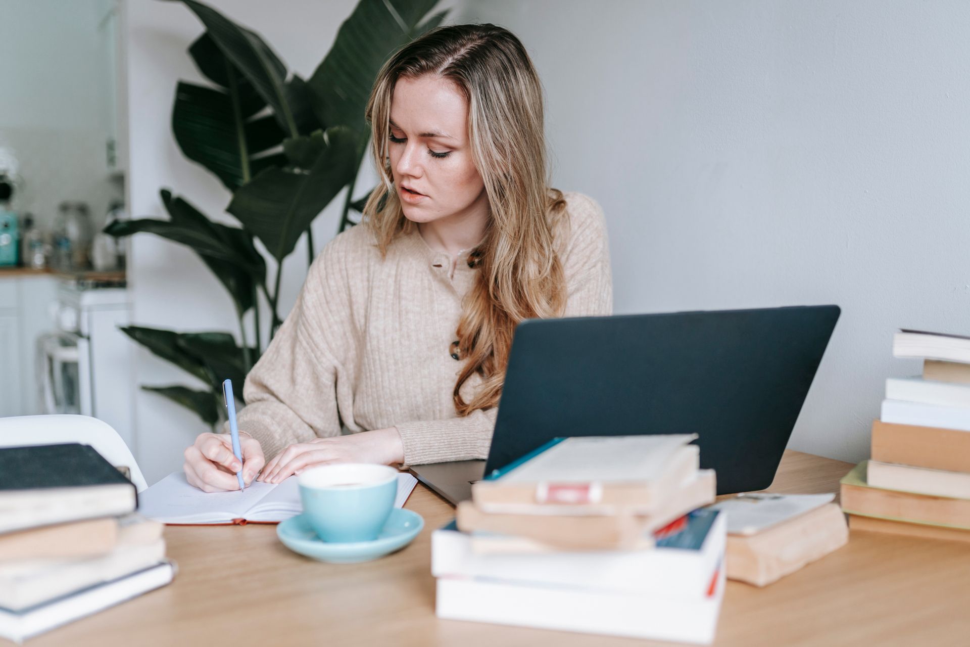 A woman creating a job search plan and taking notes in a notebook beside her laptop
