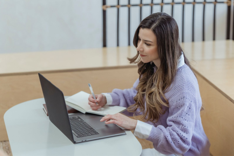 Professional woman planning her job search while using a laptop and taking notes.