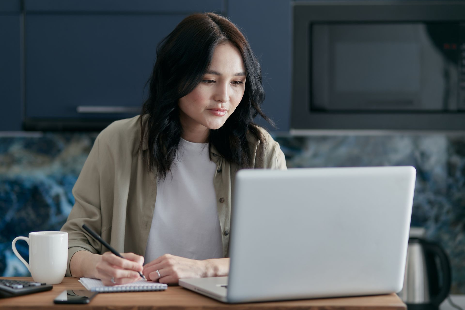 Woman taking notes while preparing a resume on her laptop